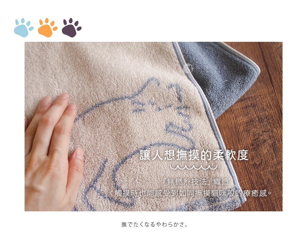 一隻手輕撫著印有貓咪圖案的淺色浴巾，浴巾質地柔軟蓬鬆，旁邊疊放著深灰色毛巾，整體呈現舒適自然的居家質感，並強調如同撫摸貓咪般的觸感與療癒氛圍。