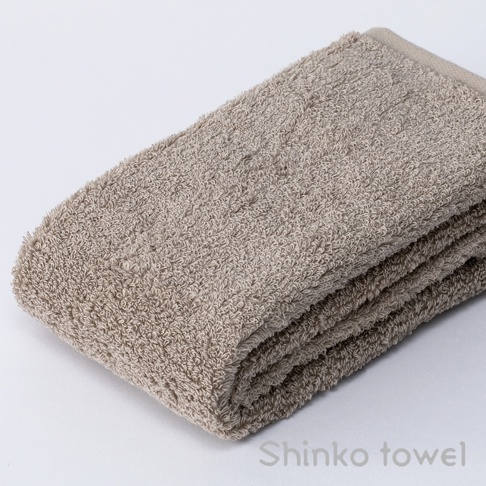 一條米色泉州匹馬棉浴巾，織紋細緻，質地蓬鬆，對折擺放在白色背景上。