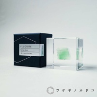 深藍色包裝盒旁，一個透明立方體內嵌著一塊綠色螢石，盒子上標有「FLUORITE」字樣及日文說明，立方體側面有「Made in JAPAN」字樣。
