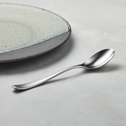 精緻的霧面不鏽鋼湯匙，搭配帶有藍色斑點和灰色邊緣的盤子，擺放在淺色大理石紋背景上。