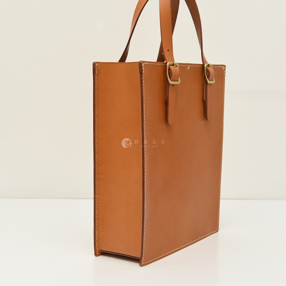 職人手作皮革商務用紙袋托特包，淺棕色，方形包身，附有兩個長提把和兩個可調節的皮帶扣。