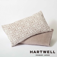 米白色菱形格紋枕套堆疊在淺褐色毛巾上， ambos 呈現柔軟的絨毛質感。