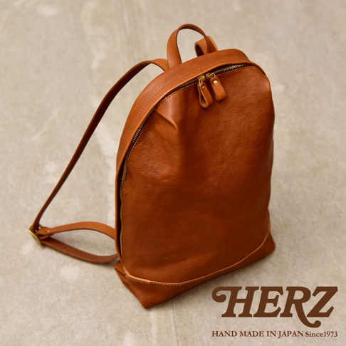 這款日本HERZ職人手作Organ系列皮革後背包，呈現簡約俐落的折皺風造型，採用質感溫潤的棕色義大利Eufrate皮革製成，包身線條柔和立體，搭配精緻金屬拉鍊與耐用的皮革背帶，展示手作職人細膩的工藝品質。