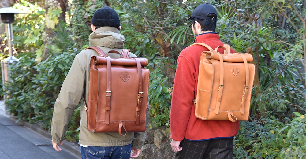 兩款棕色皮革後背包，一款為深棕色，另一款為淺棕色，均有滾邊設計、金屬扣環和可調節的皮革肩帶，適合戶外活動。