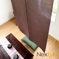 深棕色日製手作防焰門簾，垂墜於木質地板上，中央縫線明顯，質感細膩，與綠色長形坐墊和下方木製茶桌上的日式擺設形成對比。