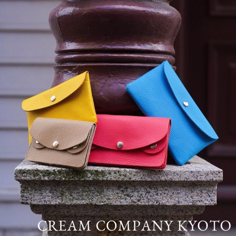 四個皮革零錢包，分別為亮黃色、卡其色、紅色和藍色，皆有銀色按扣，擺放在石質階梯上。