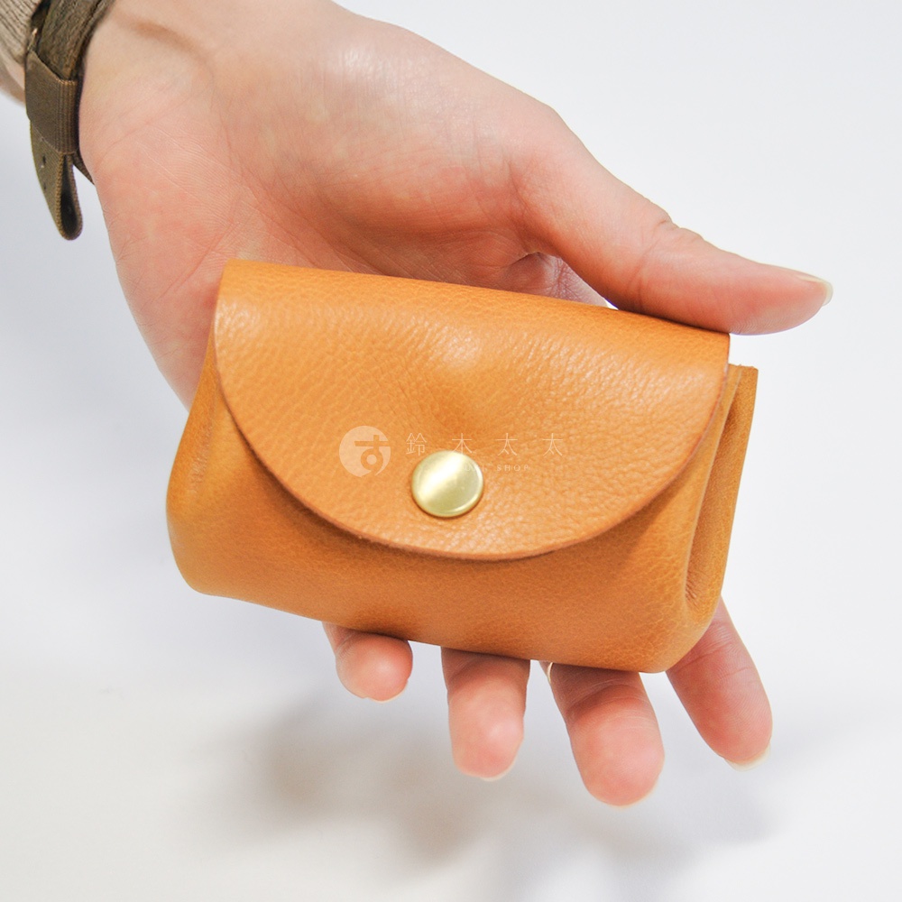 手持一個淺棕色皮革三層收納零錢包，包身帶有圓形金屬按扣，材質為天然皮革。