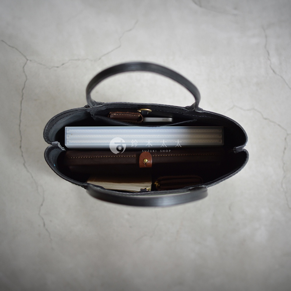 黑色皮革托特包內部，擺放著文件夾、筆記本和手機等物品，展現出包款的收納空間。