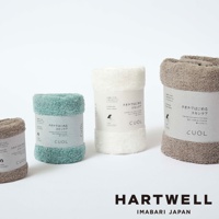 CUOL今治柔彈低摩擦美肌毛巾，共三色：淺綠、白色、淺棕色。毛巾質地柔軟，表面有細緻絨毛，捲成圓筒狀，並附有產品標籤。