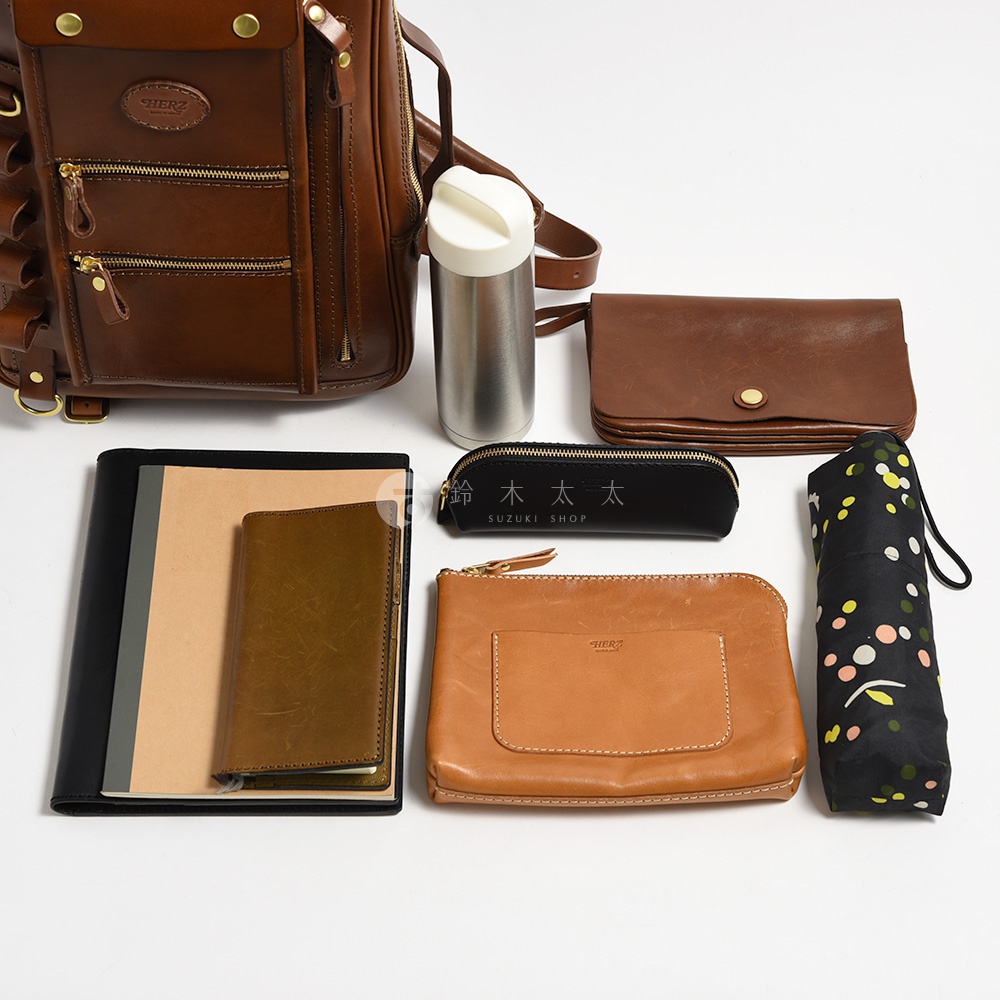 棕色皮革後背包、一個銀色保溫瓶、一個棕色皮革長夾、一個黑色筆袋、一本黑色筆記本、一本棕色筆記本、一個淺棕色皮革收納包，以及一把黑色印有彩色圓點的摺疊傘。