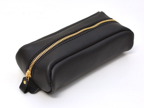 黑色皮革製成的圓角筆袋，配有金色拉鍊和皮革拉環，整體簡約大方。