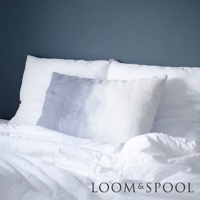 一張床鋪，上面有兩個純白色枕頭，其中一個枕頭上放著一個灰色與白色漸層的短絨枕套。