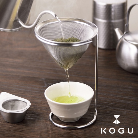 日製18-8不鏽鋼濾茶器，濾網為細網目，附有獨立支架，可過濾咖啡粉與茶葉，搭配白色茶碗使用，旁邊另有一個同材質的濾茶勺。