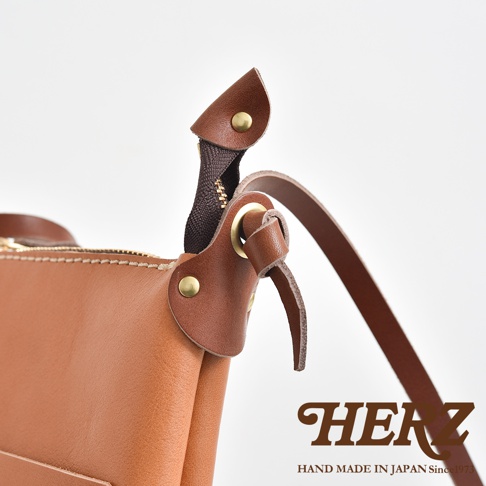 職人手作皮革直式隨身單肩包，展現自然色澤的牛皮材質，搭配黃銅五金與深棕色拉鍊，細節處以皮革包覆拉鍊頭，風格簡約。