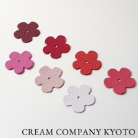 京都職人手作的五款皮革花朵裝飾，顏色包含紅酒紫、桃紅、櫻桃紅、淺粉和白色，皮革表面有細緻紋理，每朵花中央皆有一圓孔。