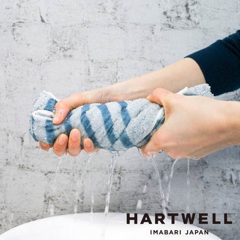 雙手擰著一條藍白條紋的今治毛巾，水從毛巾中流出，展現其高吸水性。