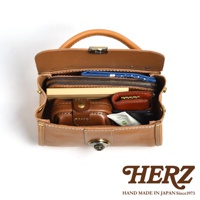 職人手作皮革迷你手提包，標誌性焦糖色皮革，設計簡約，內有隔層，可收納鑰匙包、小錢包、化妝品和紙製品。包款上方配有提把，前方設有金屬鎖扣，整體風格經典復古。