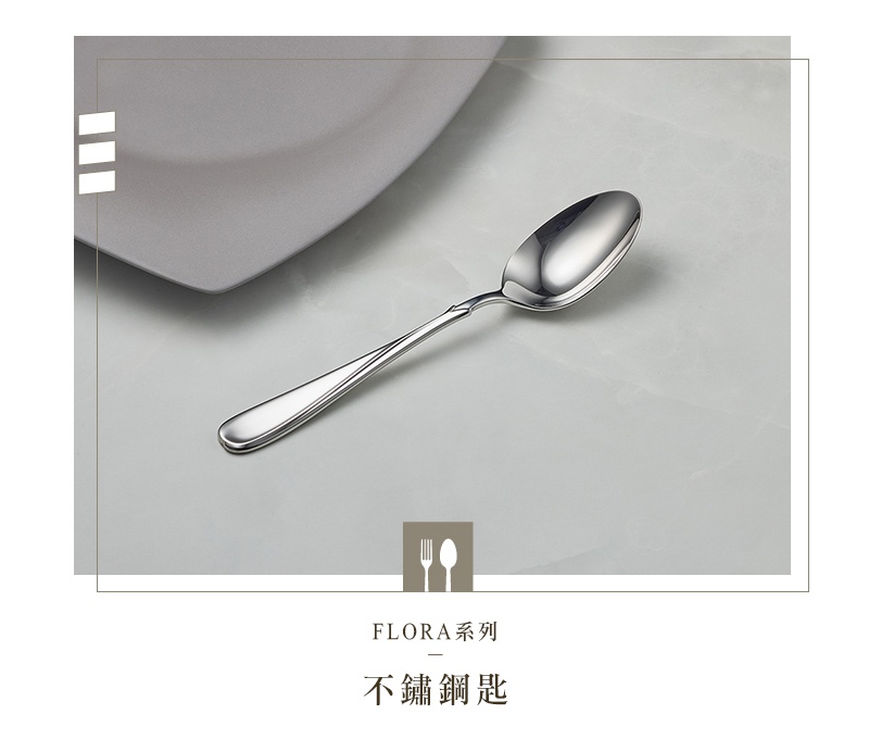 Flora系列不鏽鋼湯匙，湯匙為銀色金屬材質，湯匙頭呈橢圓形，柄部有簡潔的曲線設計，湯匙放置在灰色的盤子一角旁，背景為淺灰紋理桌面。