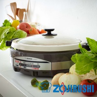 象印土鍋風鐵板萬用鍋 EP-RAF45，鍋身為深棕色與米白色，搭配透明玻璃鍋蓋，鍋蓋中央有黑色把手。鍋身側邊有顯示溫度與功能的控制面板，周圍擺放著新鮮的蔬菜水果，如高麗菜、花椰菜、番茄、蘋果、檸檬和胡蘿蔔。