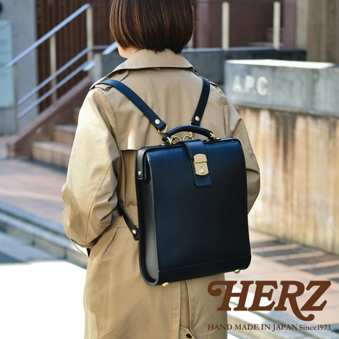 職人手作黑色皮革杜勒斯商務後背包，方形設計，配有金色鎖扣與提把，皮革材質，黑色肩帶。