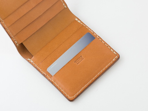 職人手作皮革二折直式小短夾，採用天然棕色皮革，內有數個卡槽，夾層中插入一張金屬色卡片，車縫線清晰。