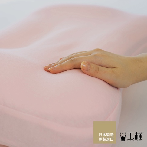 一隻手輕柔地觸碰著柔軟的粉紅色枕頭，枕套材質看起來是棉質。