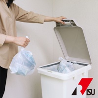 一個人正將一個裝有垃圾的透明塑膠袋投入一個米白色的大容量垃圾桶。垃圾桶蓋是打開的，呈現米灰色。