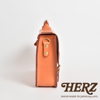 側邊視角，展示一個橙棕色皮革製成的方形公事包，包體側面有兩個銅製鉚釘和一個金屬扣環，包包上方有提把，整體為簡約設計。