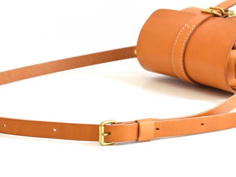 職人手作皮革皮扣單肩包，採用棕色皮革材質，設有可調節的皮革背帶和金屬皮扣，展現簡約時尚的風格。