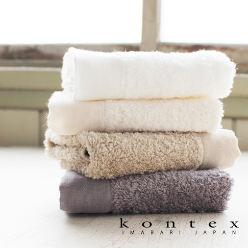 疊放的 PRIMAVERA 超細纖純棉毛巾，從上至下顏色依序為白色、米白色、淺棕色和淺灰色，毛巾質地蓬鬆柔軟。