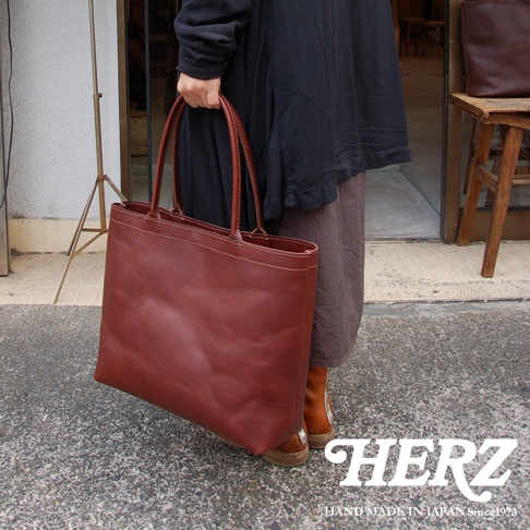 一個人手提一個棕色皮革托特包，包包的縫線清晰可見。