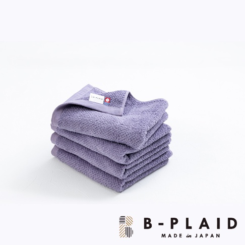 疊放的紫色薄手鱗紋毛巾，質感柔軟，帶有品牌標籤。