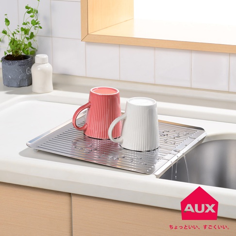 不銹鋼方形瀝水籃，上面放著一個粉紅色和一個白色的條紋馬克杯，瀝水籃傾斜，水正流入水槽。