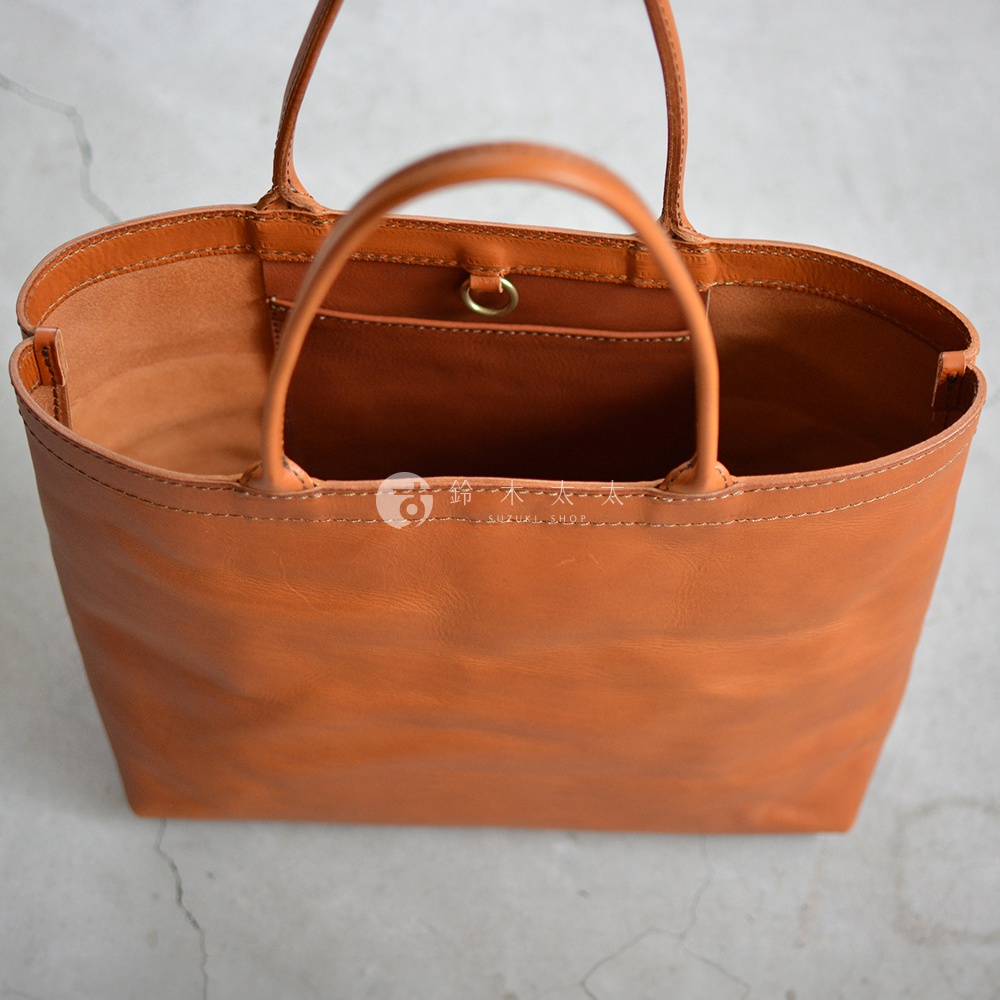 一個棕褐色的皮革托特包，有兩個提把，包包內部有一個小口袋，包包的縫線清晰可見。