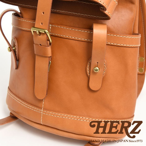 職人手作皮革雙口袋折蓋後背包，展示為棕褐色皮革材質，車縫線清晰，配有黃銅色金屬釦件，設計簡潔實用。