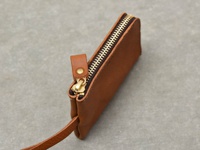 職人手作的淺棕色皮革鑰匙包，配有黃銅拉鍊和皮革拉環，整體簡潔實用。