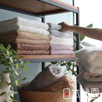 堆疊的飯店浴巾，從上往下顏色分別為白色、淺灰色、白色、淺紫色、白色，以及左側堆疊的白色、卡其色、褐色、深褐色浴巾。右側另有堆疊的白色、淺灰色浴巾，以及籃子中捲起的淺灰色、卡其色浴巾。