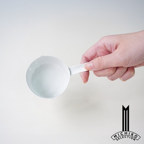 手持白色琺瑯量杯，杯中有少量水，背景為淺色。