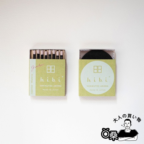 一盒綠色紙盒裝有十支香氛火柴，火柴頭為粉紅色。旁邊是另一盒相同設計的綠色紙盒，內有一個黑色圓形物體，盒蓋為透明塑膠。