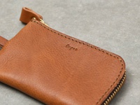 職人手作皮革Organ抽繩收納鑰匙包，採用棕褐色皮革製成，帶有質樸紋理，頂部有抽繩開合設計，並配有金色拉鍊及品牌Logo壓印。