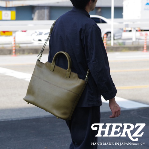 職人手作皮革大容量兩用托特包，採用橄欖綠皮革製成，設有雙提把與可拆卸肩背帶，包身有縫線裝飾，設計簡約大方。