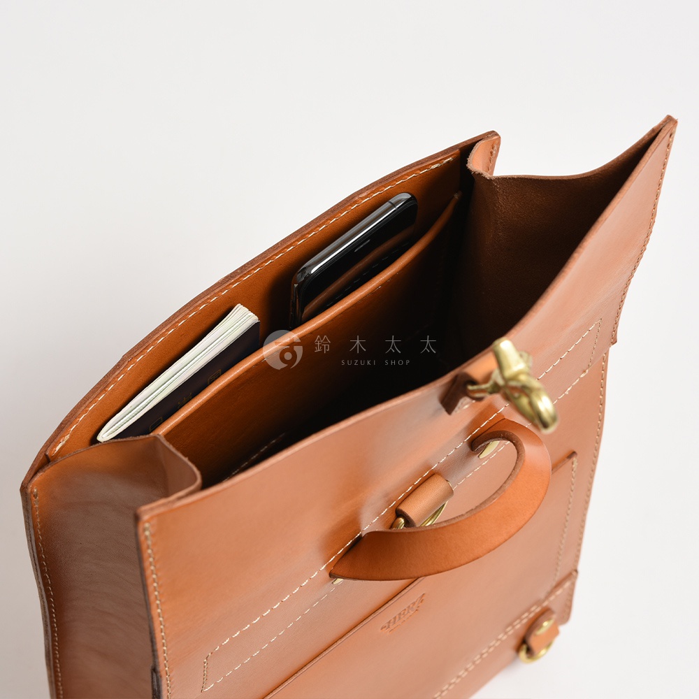 職人手作皮革紙袋風後背包，棕色皮革，內有手機與薄冊，包包內部結構清晰，做工精緻。