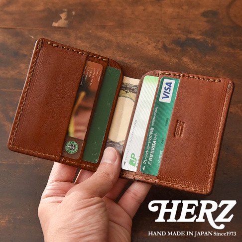 HERZ 品牌手作皮革薄型卡片鈔票夾，展示於木紋背景上，夾內放有VISA金融卡和日圓鈔票。