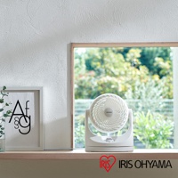 白色IRIS OHYAMA PCF-MKM15空氣循環扇，具有可調節角度的圓形扇頭，置於窗邊木質檯面上。