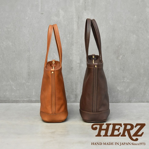 兩款皮革手提包，一款為淺棕色，另一款為深棕色，皆呈現簡約托特包的造型，並有品牌標誌 HERZ。