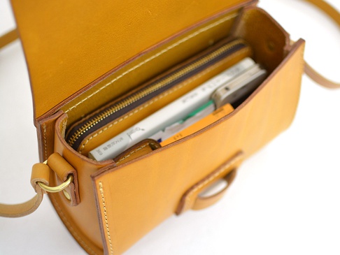 職人手作皮革寬扣帶馬鞍包 (CP-1)，此款馬鞍包為淺棕色，採用真皮革材質，包包頂部翻蓋打開，露出內部空間，可容納手機、書籍等物品。包包配有黃銅色金屬扣環和拉鍊。