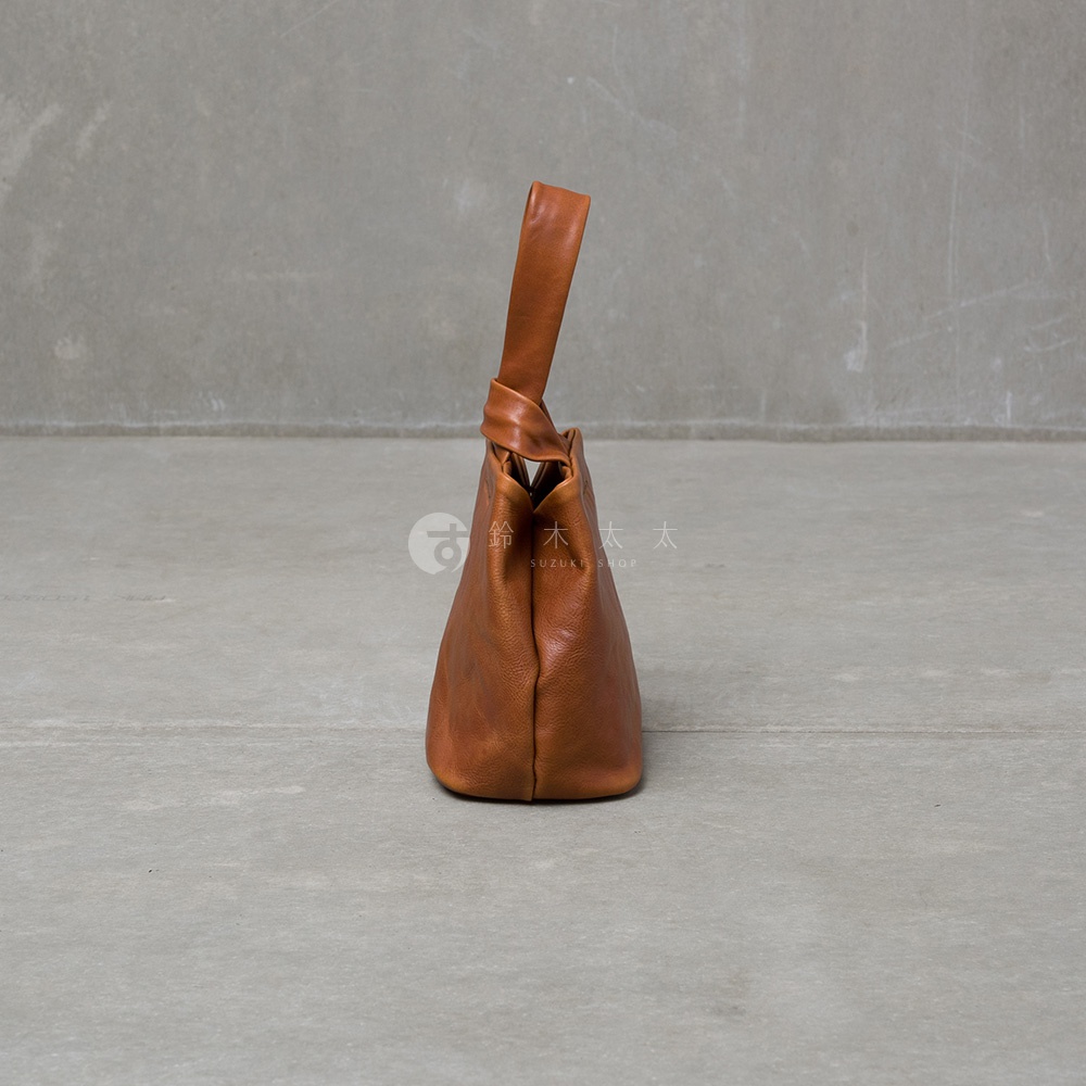 棕色皮革單柄手提包，以簡約的設計風格呈現，包身呈現自然的皮革紋理，提把處有一個打結的造型，為包款增添細節。