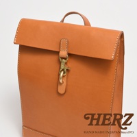 職人手作皮革紙袋風後背包，採用天然皮革材質，呈現自然棕色調，包款設計簡約，附有金屬釦環與皮革束帶，適合日常攜帶。