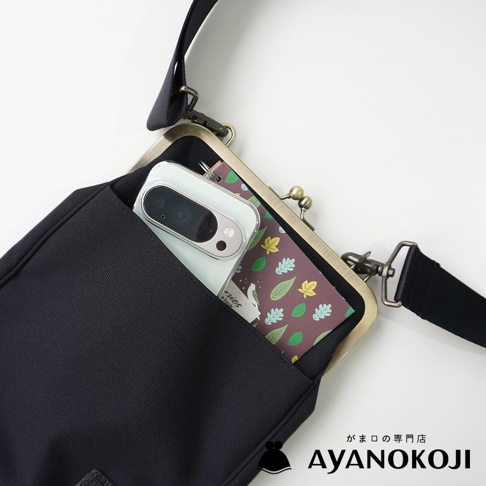 京都職人手作 AYANOKOJI Sarei機能布直式口金斜背包，展示一個黑色斜背包，包內有一部手機和印有葉子圖案的卡片。