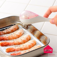 手持白色帶粉紅色半透明蓋子的leye料理專用撒粉器，正將白色細粉均勻撒在不銹鋼烤盤中的鮮蝦上。